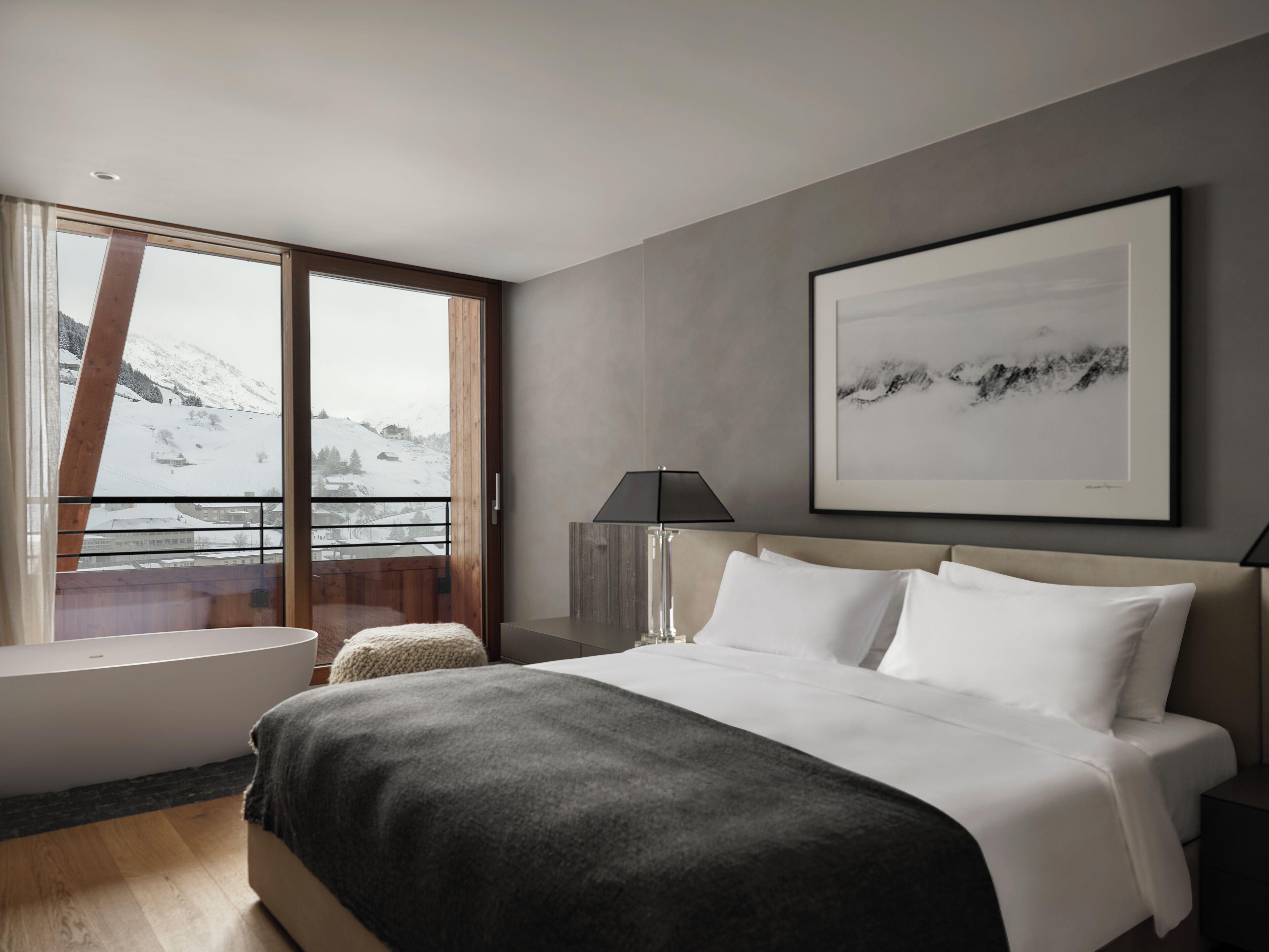A modern bedroom with a large bed, a bathtub, and a view of a snowy mountain landscape.