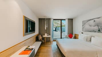 Habitación de hotel moderna con una cama grande, un área de descanso con una mesa y un balcón con vistas a las montañas.