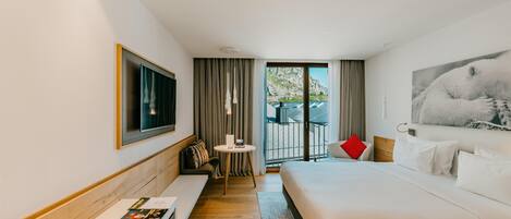Habitación de hotel moderna con una cama grande, un área de descanso con una mesa y un balcón con vistas a las montañas.
