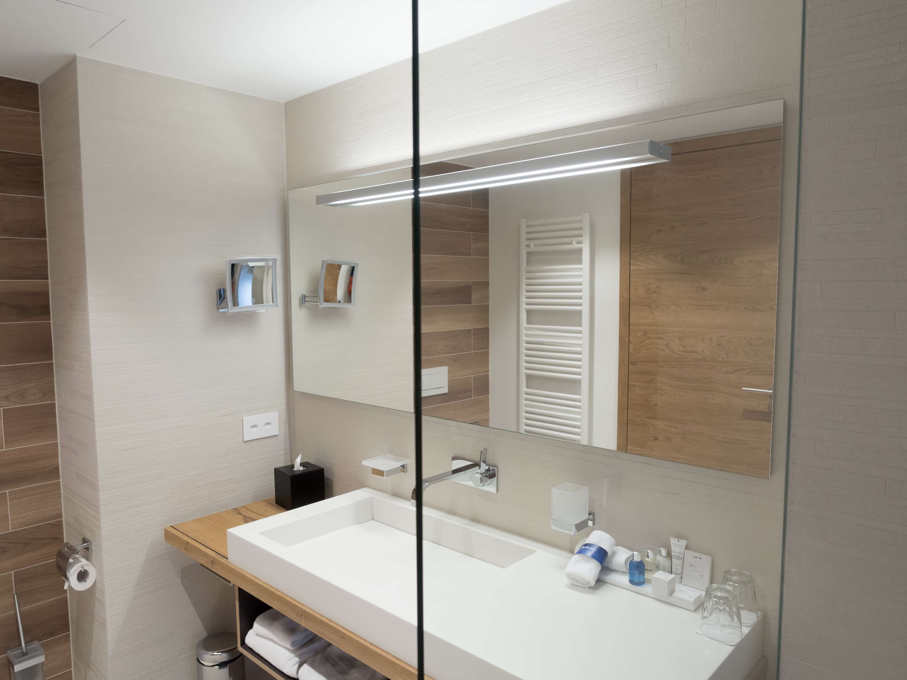 Un baño moderno con un espejo grande, un lavamanos blanco y un mueble de tocador de madera.