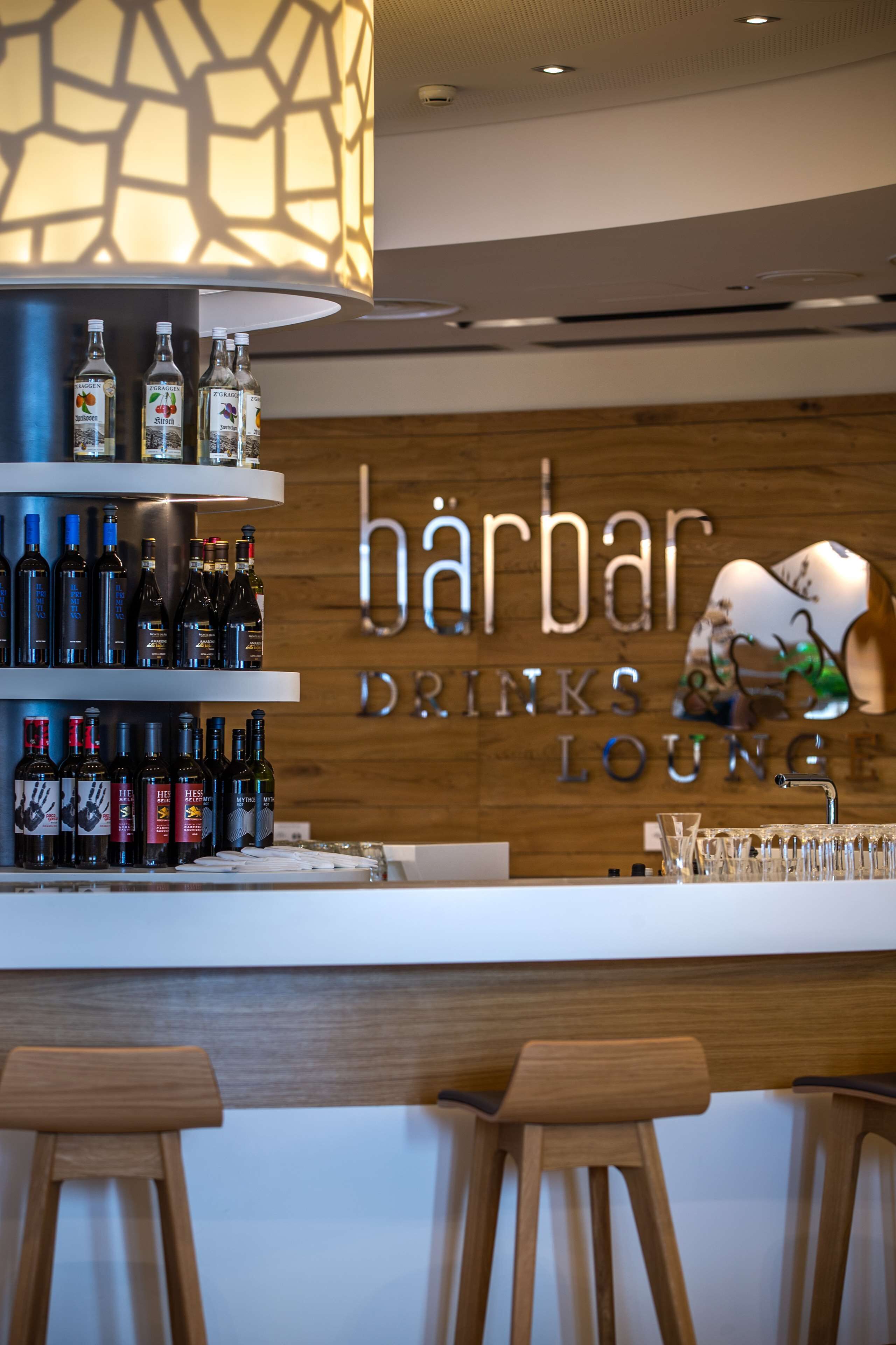 A bar area with shelves of bottles, a sign reading "barbar drink lounge", and wooden stools.