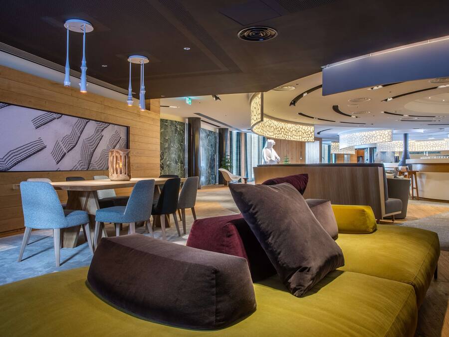 Eine moderne Hotelhalle mit einem Holzbüro, einem Essbereich mit blauen Stühlen und einer Sitzecke mit gelben und braunen Sofas.
