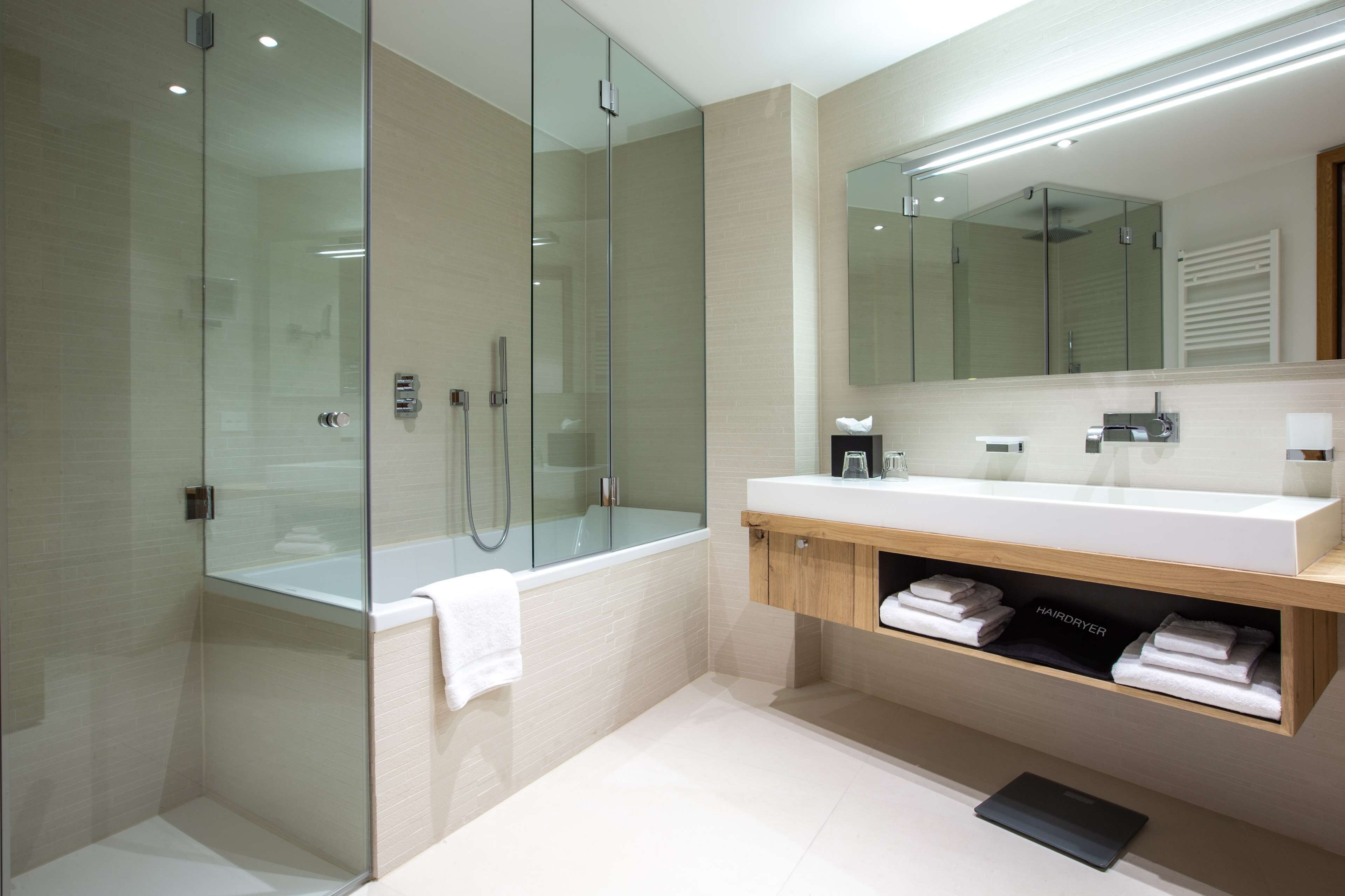 Un bagno moderno con cabina doccia in vetro, uno specchio grande e un mobile lavabo in legno con asciugamani.