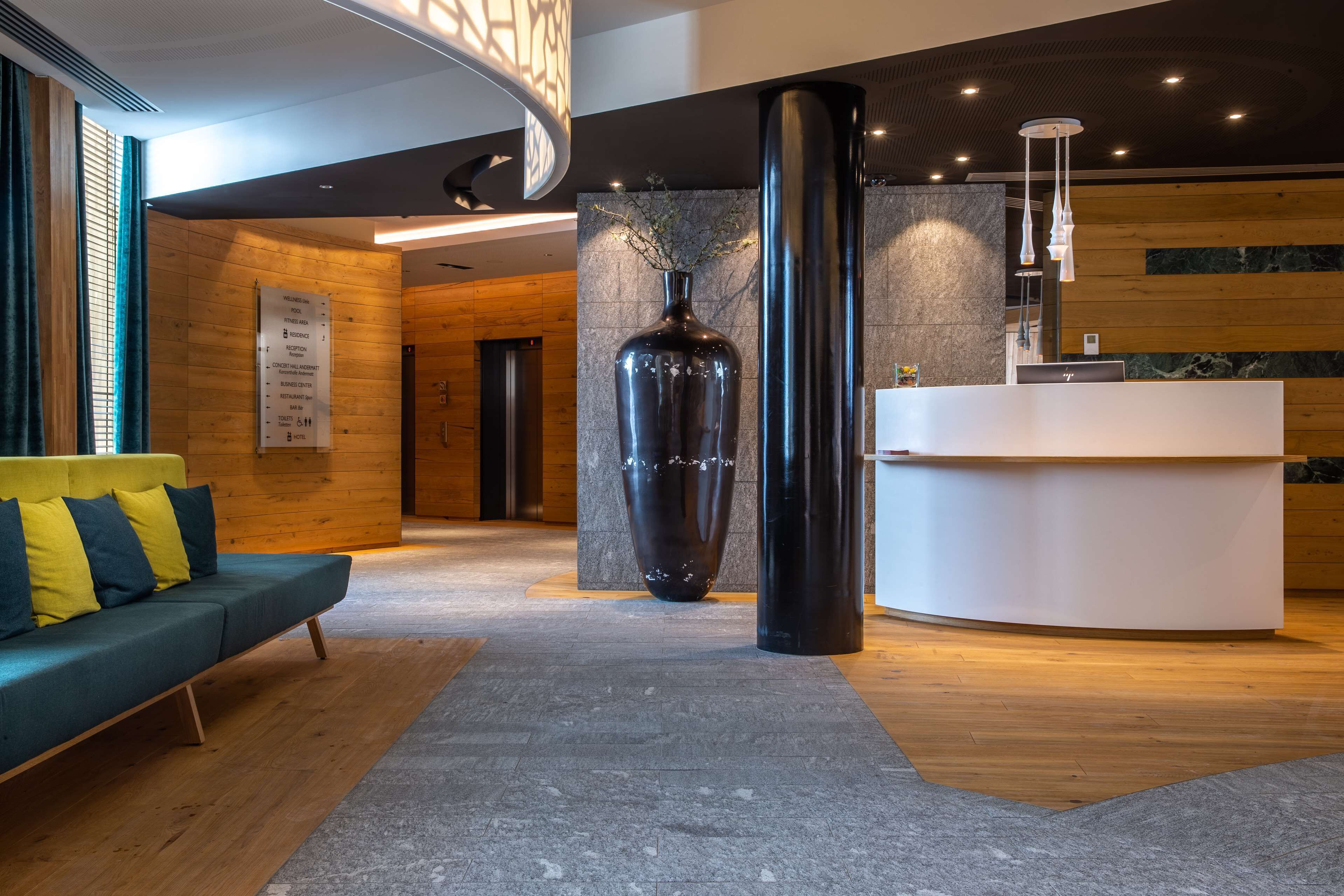 A modern lobby with a reception desk, a large vase, a sofa with cushions, and a wooden wall.