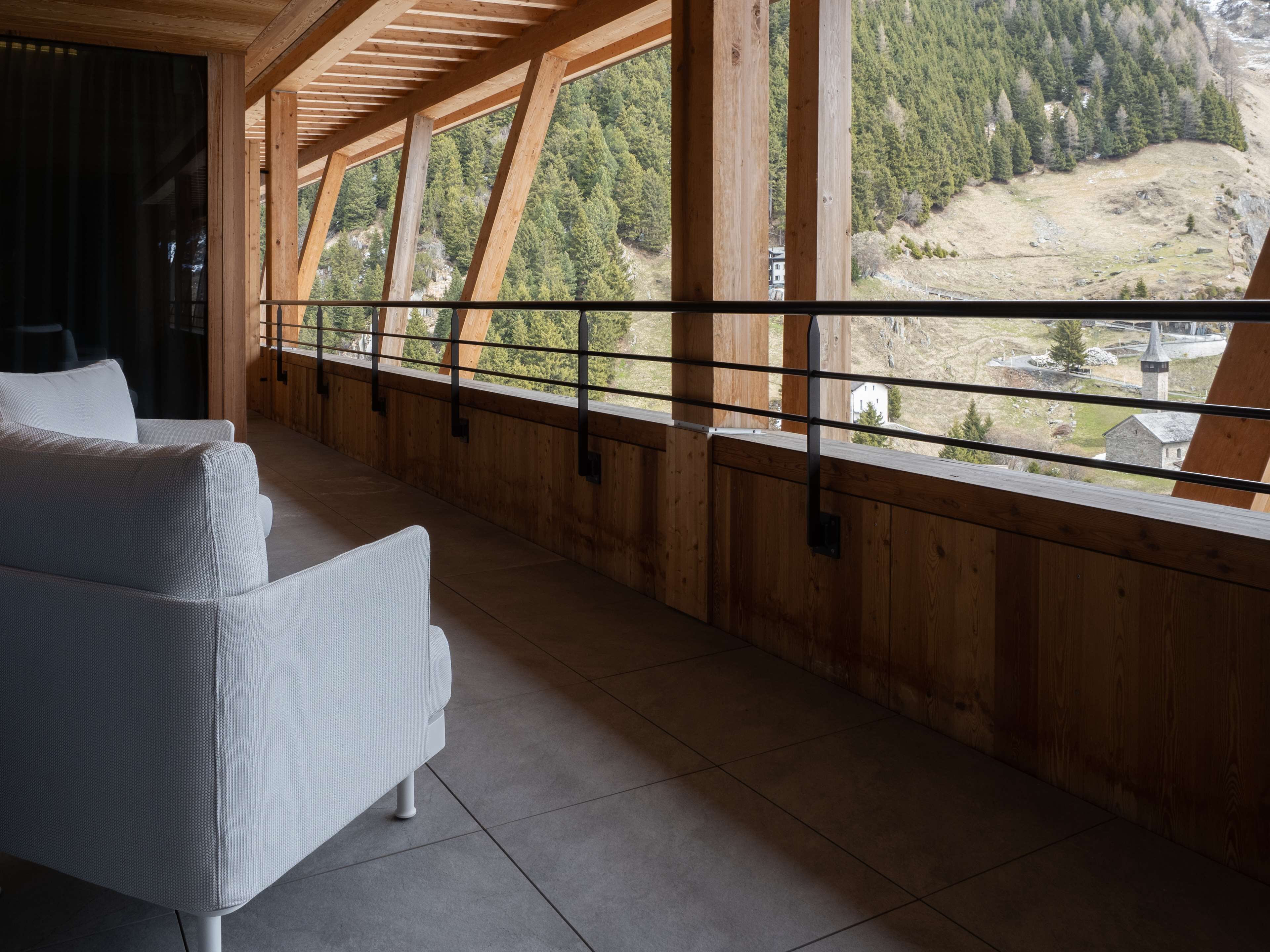 Un balcón de madera con un sofá blanco, que ofrece vistas a un valle boscoso.