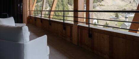 Un balcón de madera con un sofá blanco, que ofrece vistas a un valle boscoso.