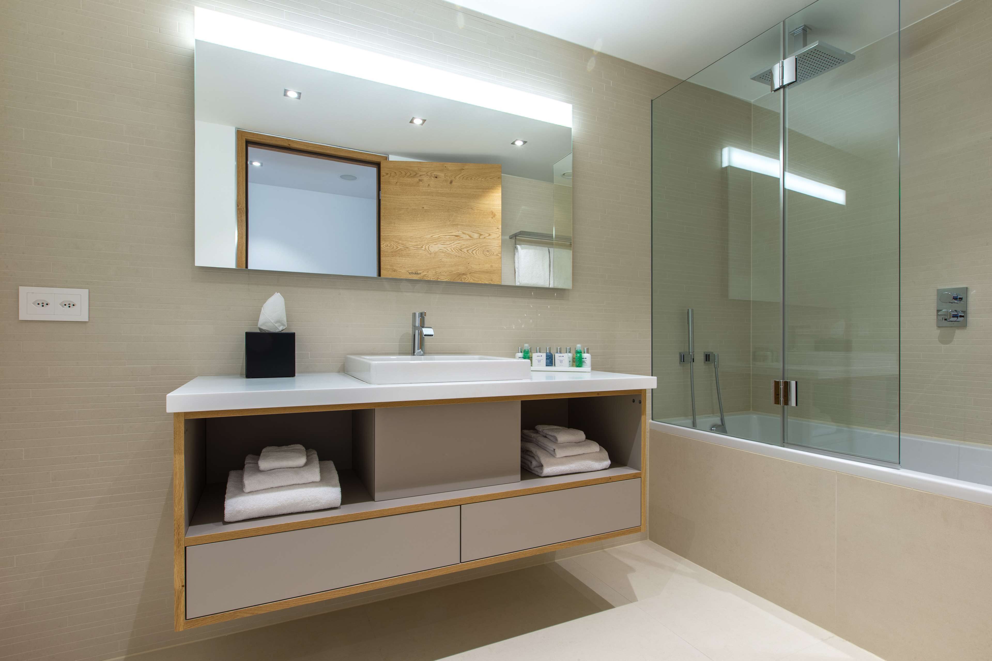 A modern bathroom with a glass-enclosed shower, a white sink with a wooden vanity, and a large mirror above the vanity.