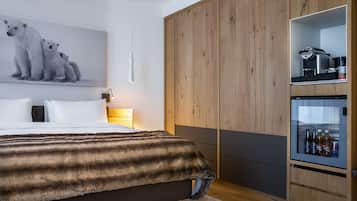 A modern bedroom with a large bed, a wooden wardrobe, and a minibar.