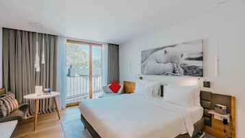 Una habitación de hotel moderna con una cama grande, una mesita redonda, un sofá y un balcón con cortinas.