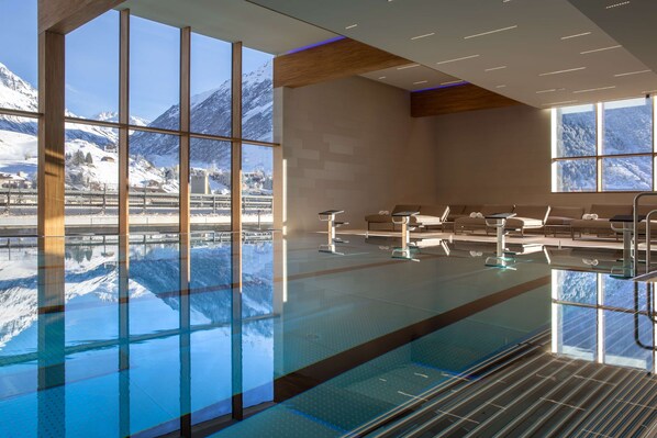 Una piscina interior moderna con amplias ventanas que ofrecen vistas a montañas cubiertas de nieve.