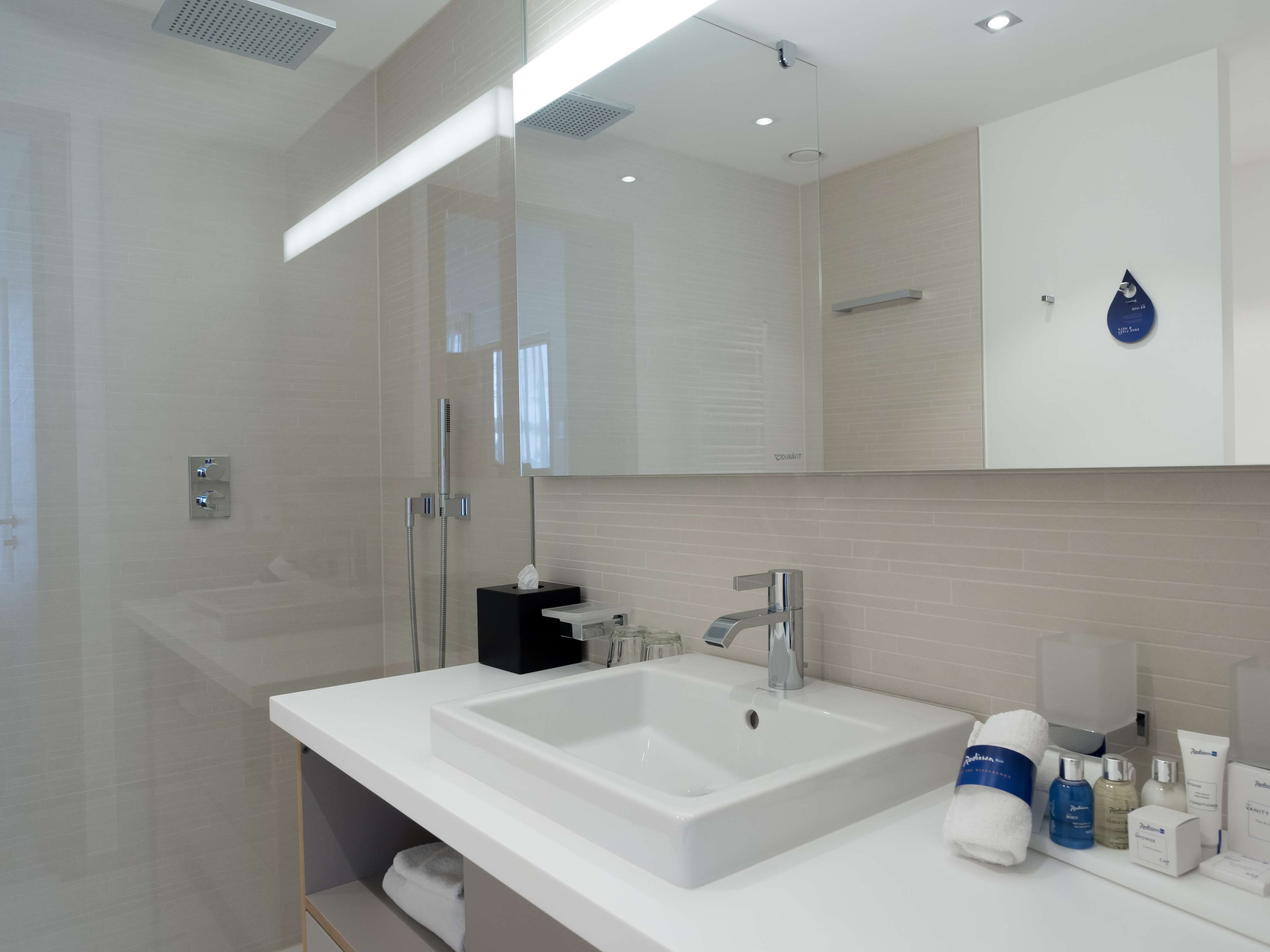 A modern bathroom with a large mirror, a white sink, and a shower area.