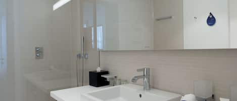 A modern bathroom with a large mirror, a white sink, and a shower area.
