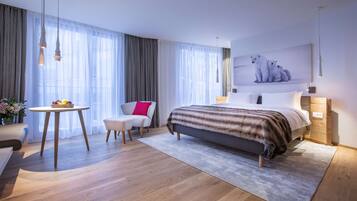 A modern hotel room with a large bed, a desk with a chair, a small table with fruits, and a painting of polar bears on the wall.