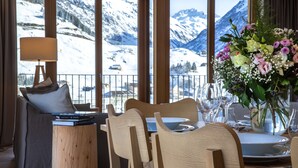 Un comedor con sillas de madera y una mesa para dos, con vistas a un paisaje montañoso cubierto de nieve.
