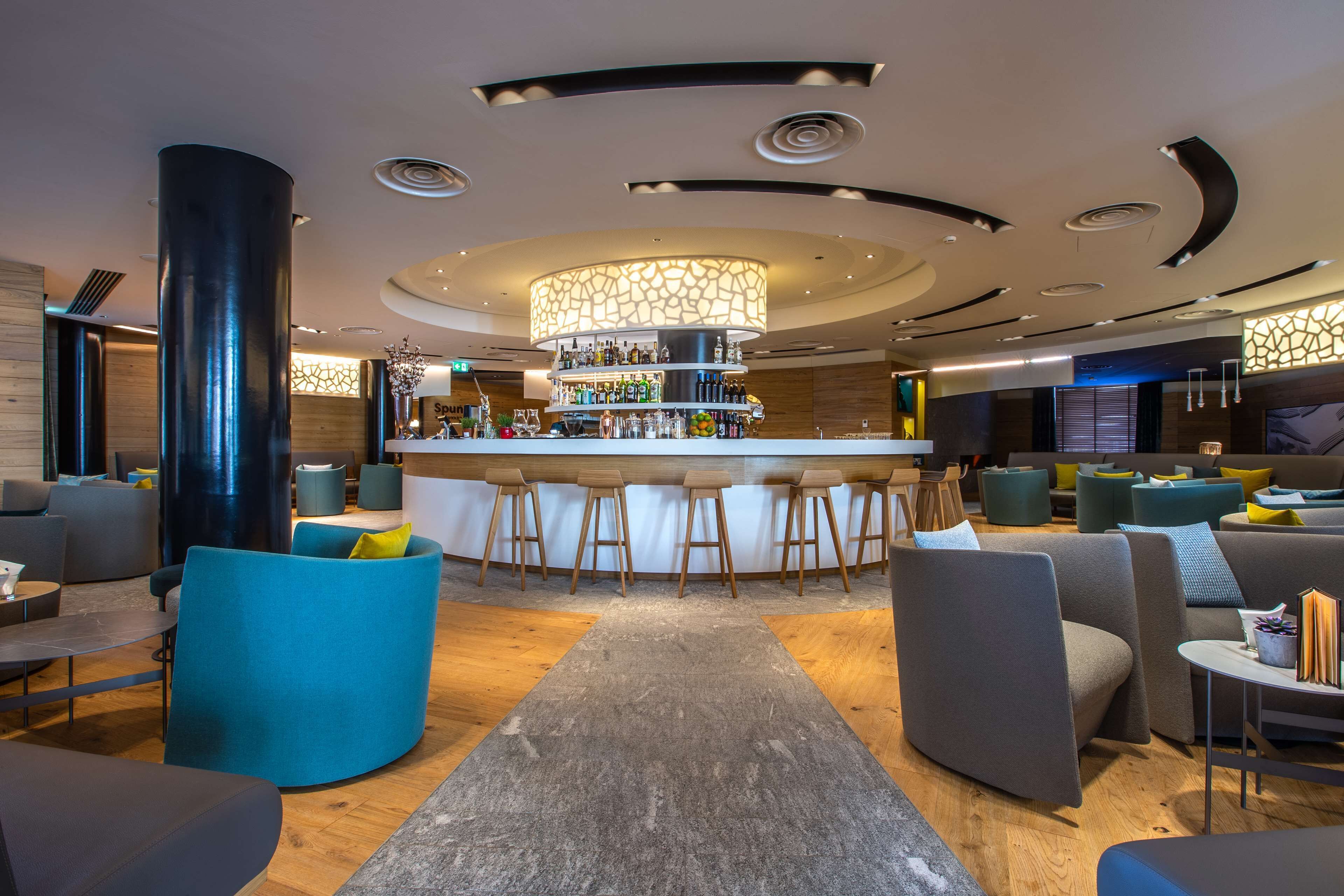 Un espace bar moderne doté d’un bar central, de sièges avec des tabourets et d’un plafond décoratif.