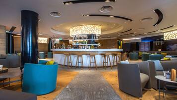 Un espace bar moderne doté d’un bar central, de sièges avec des tabourets et d’un plafond décoratif.