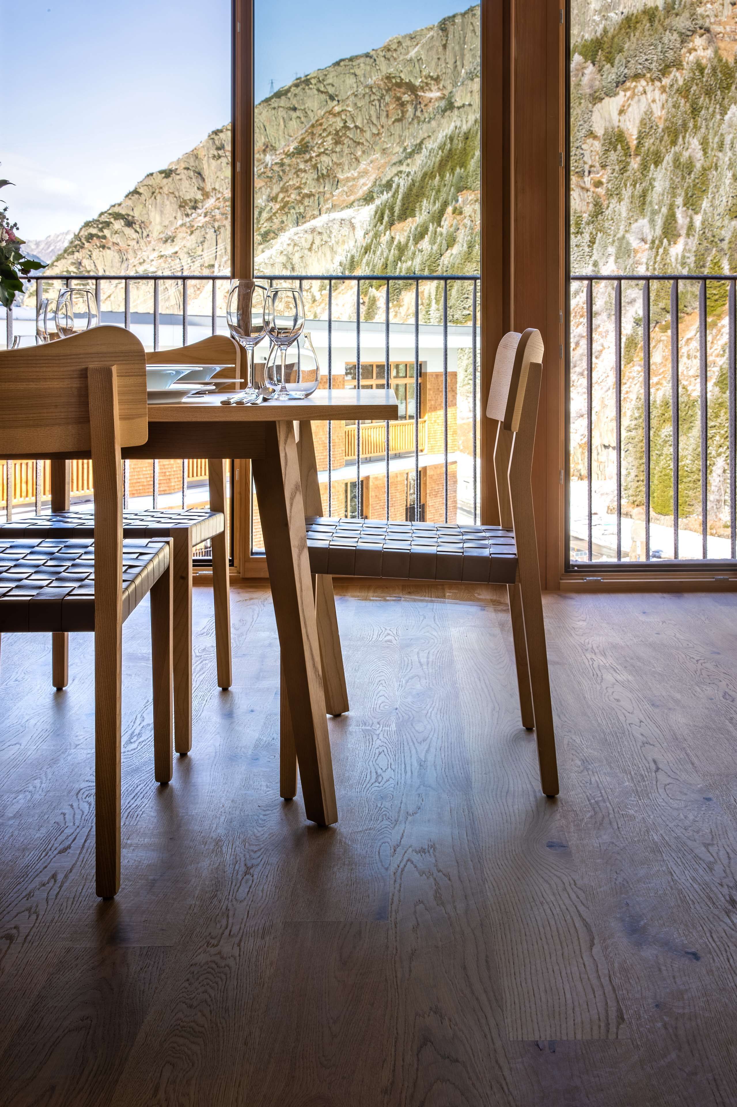 A wooden dining table with chairs, large windows with a mountain view, and a balcony railing.