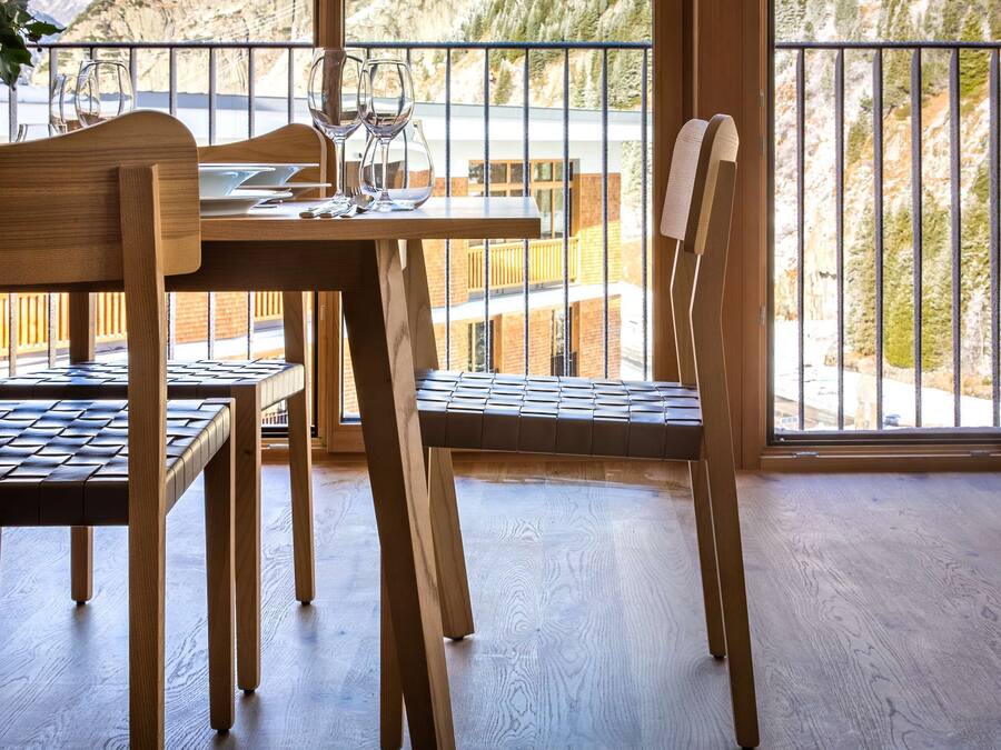 A wooden dining table with chairs, large windows with a mountain view, and a balcony railing.