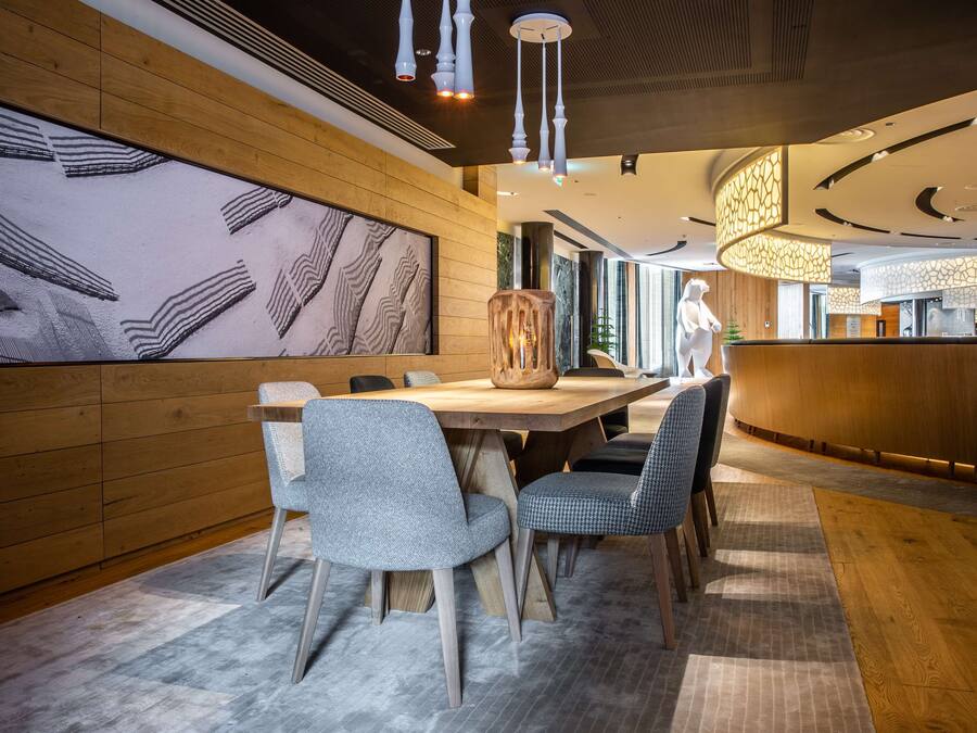 A modern interior with a wooden panel wall, a large abstract artwork, a wooden dining table with chairs, and a curved reception desk.