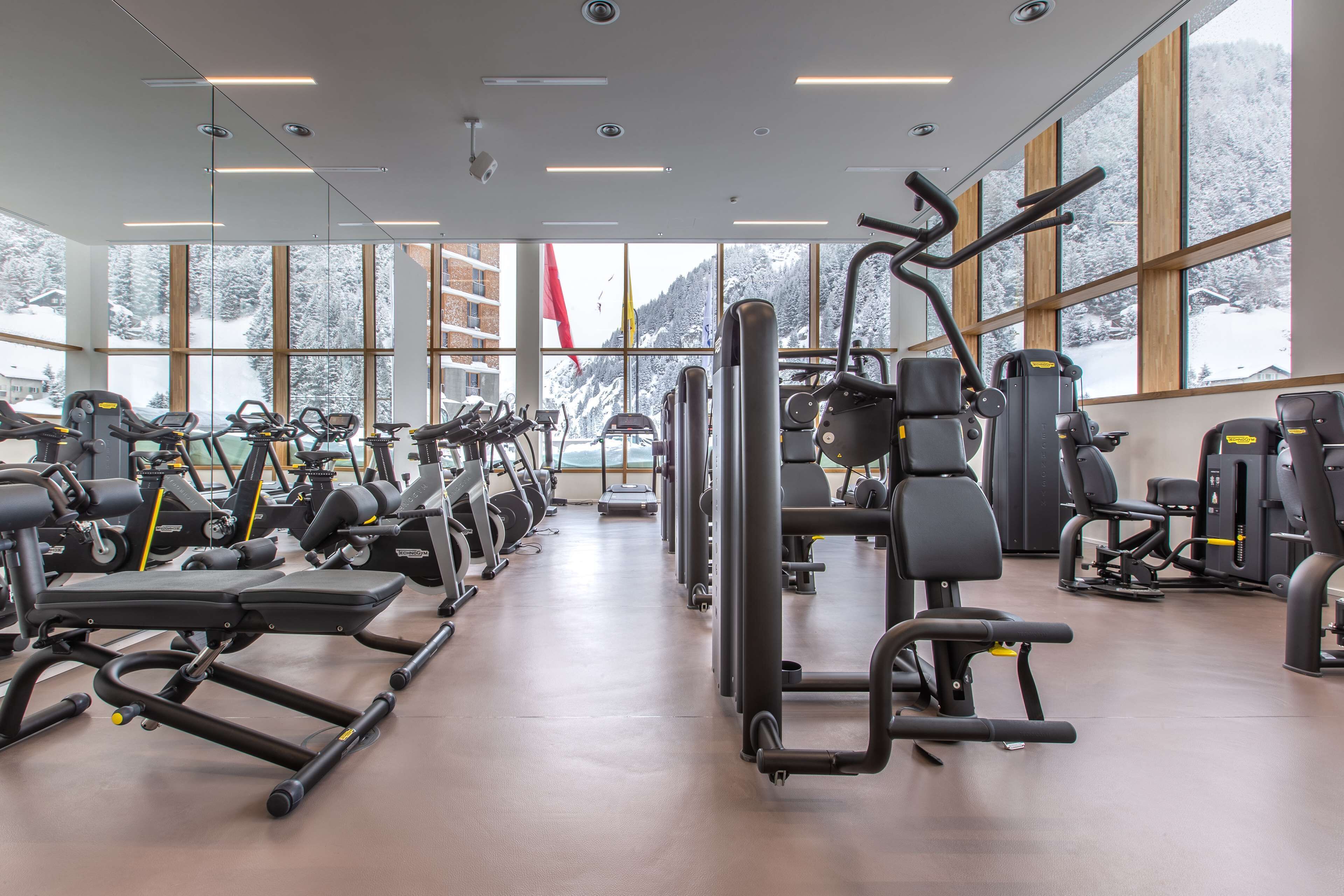A gym with various exercise equipment, large windows, and a view of snow-covered mountains.