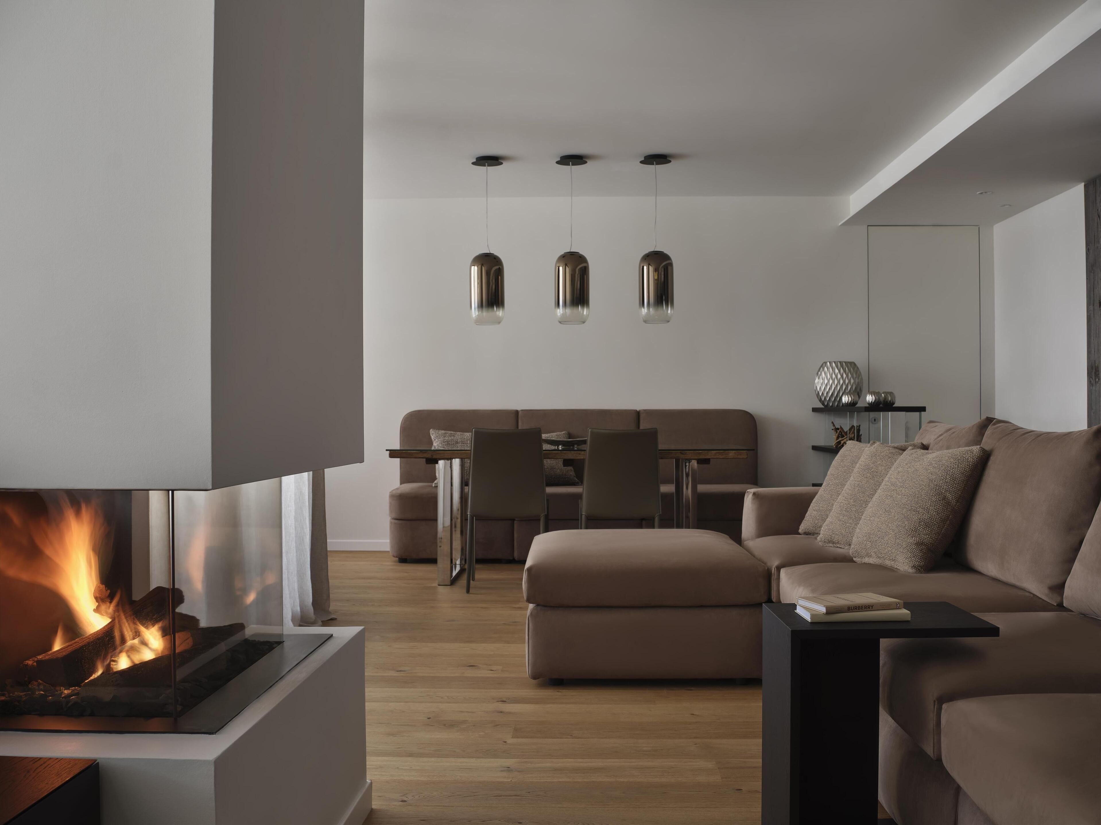 Ein modernes Wohnzimmer mit Kamin, einer Couch, einem Essbereich mit Tisch und Stühlen sowie Pendelleuchten.