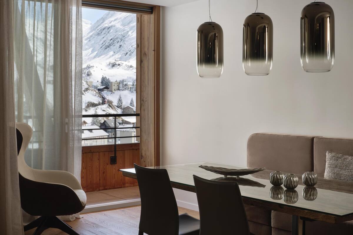 A modern dining area with a glass table, chairs, a sofa, and pendant lights.