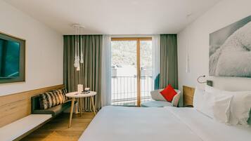 A hotel room with a bed, a sofa, a small table, and a balcony with curtains.