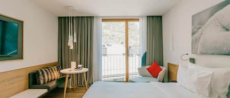 A hotel room with a bed, a sofa, a small table, and a balcony with curtains.