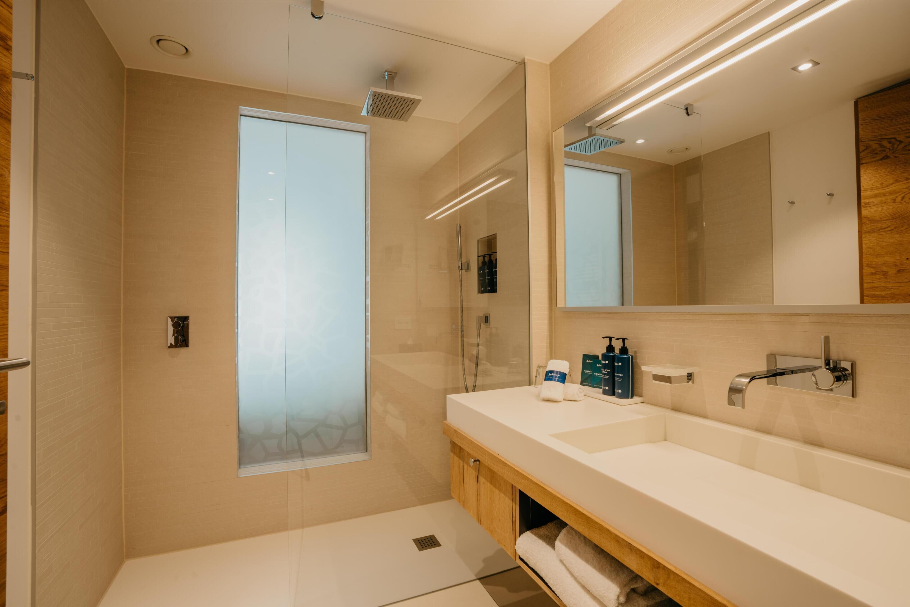 Un baño moderno con cabina de ducha de vidrio, un espejo grande y un tocador doble.