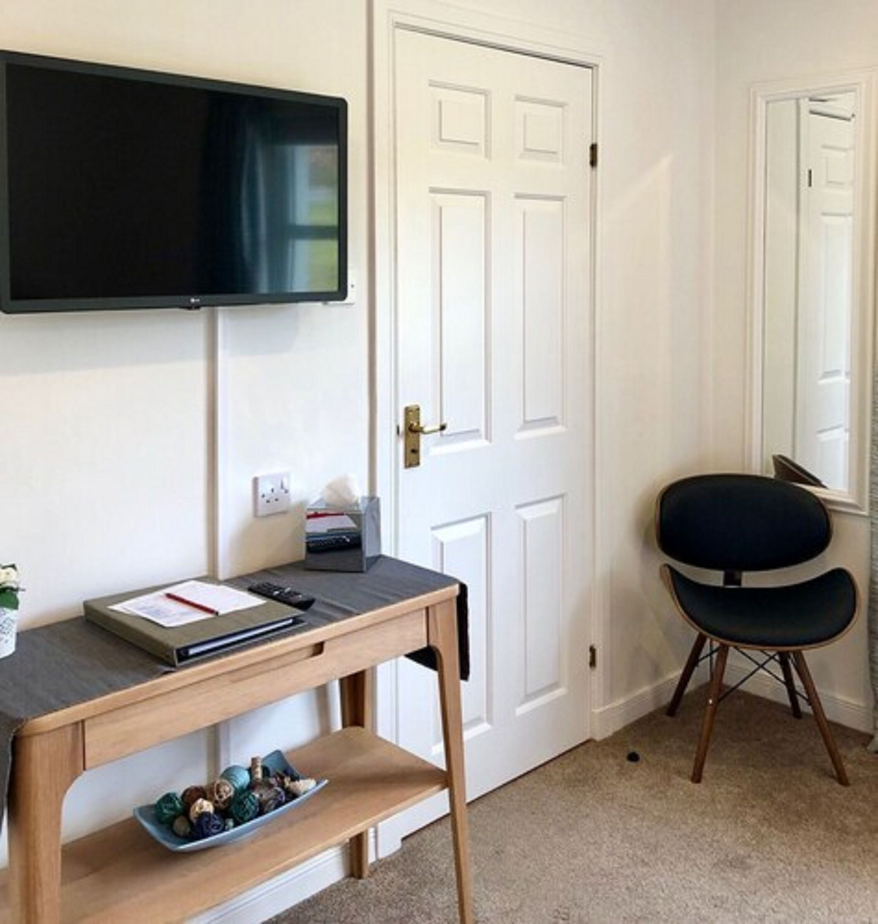 A room with a desk, a chair, a television mounted on the wall, and a door.