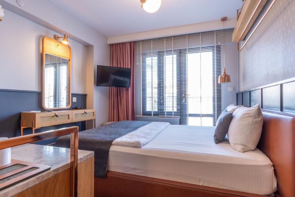 Ett hotellrum med en säng, ett skrivbord, en tv och ett fönster med persienner.
