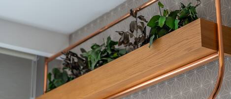 A wooden shelf with plants against a geometric patterned wall.