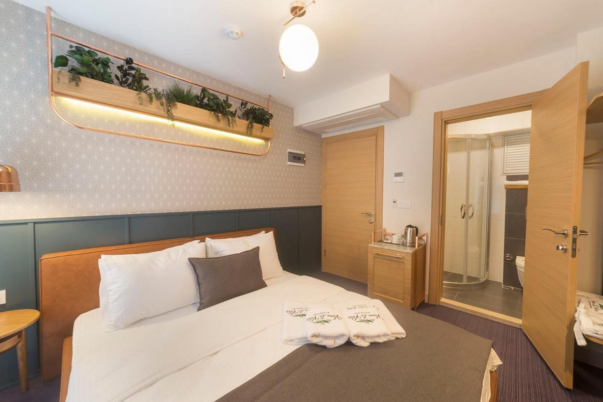 A hotel room with a bed, bedside table, a mirror, a shower, and a door.