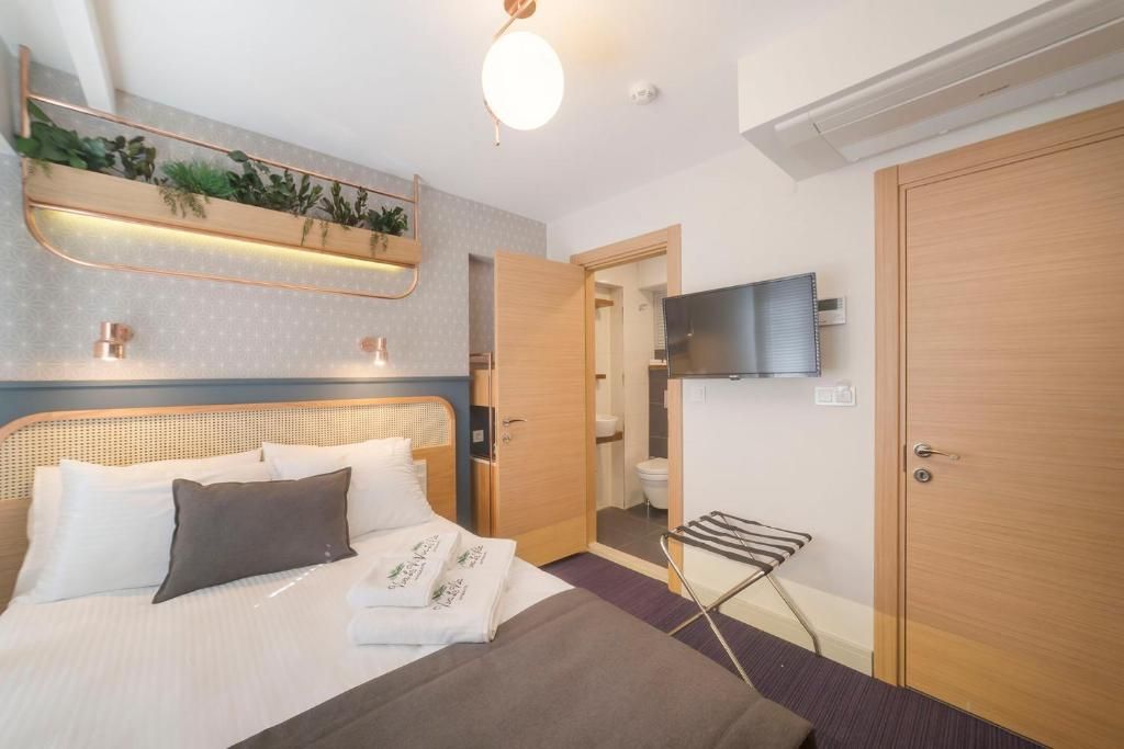 Habitación de hotel con cama, televisión montada en la pared, puerta de madera y toallero con plantas.