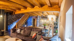 A cozy living room with a stone staircase, wooden beams, and a fireplace. - Cal Batlle Casa Rural (La Cortinada)