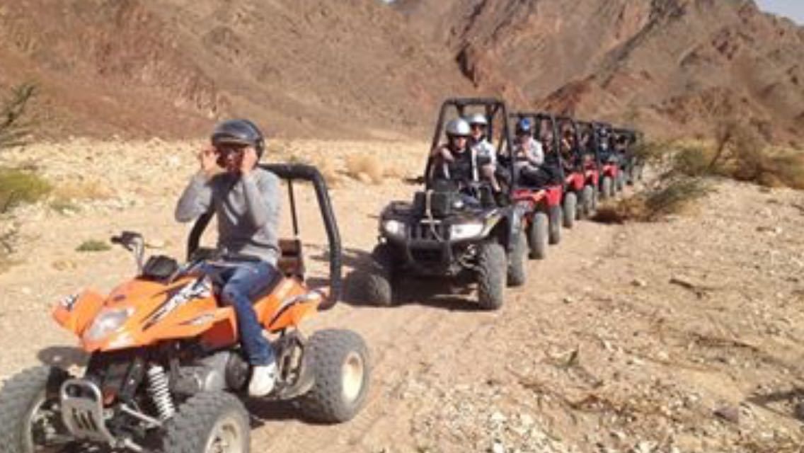 A group of off-road vehicles on a dirt path in a desert-like environment.