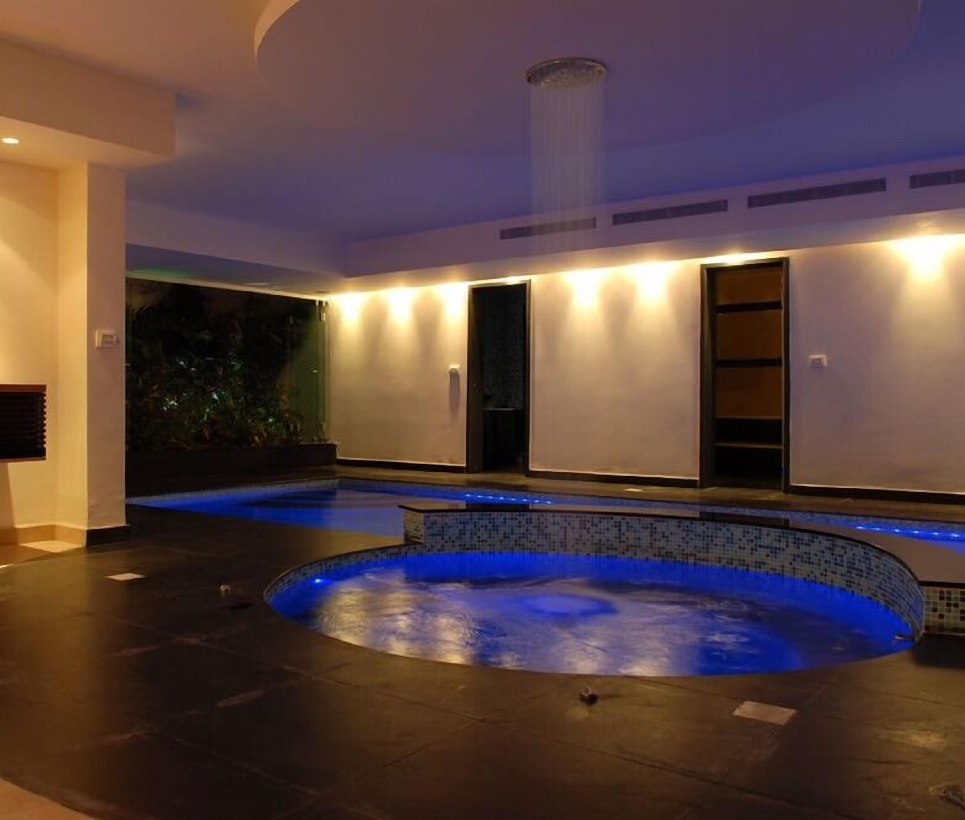 Ein Wellnessbereich mit einem runden Whirlpool, einem großen Fenster und einer Decke mit Einbaustrahlern.