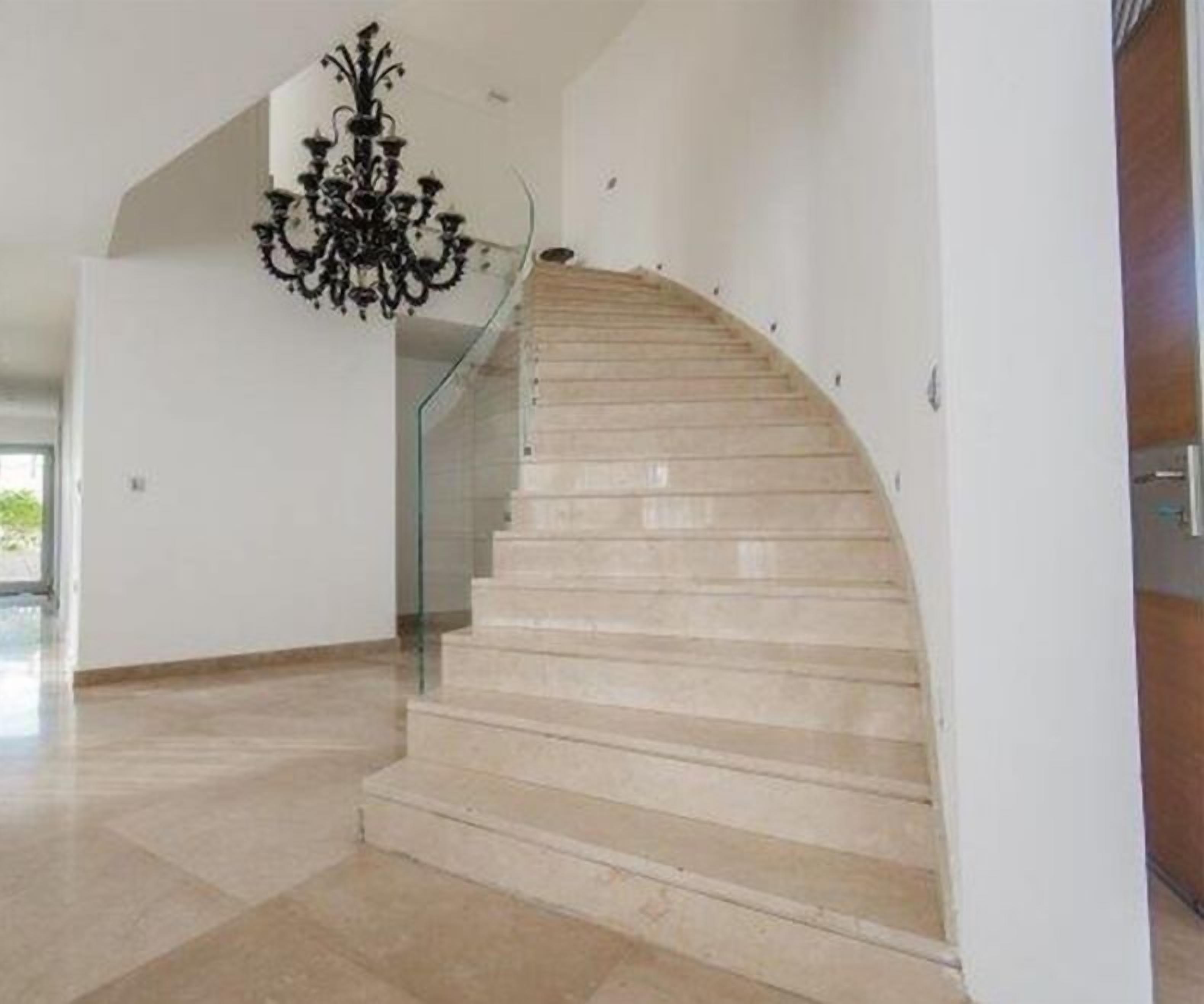 Een modern interieur met een gebogen trap, een glazen balustrade en een kroonluchter.