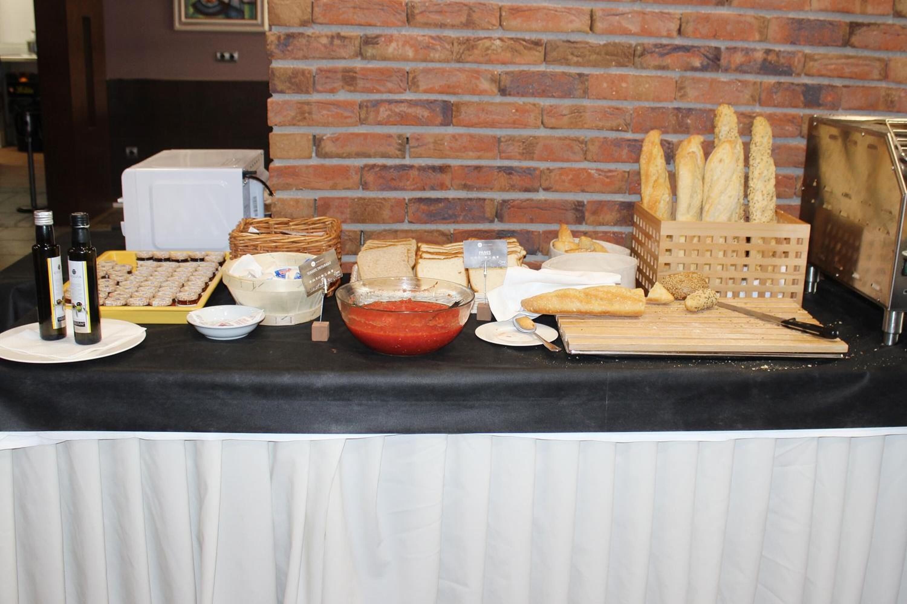 Una mesa de buffet con diversos alimentos, entre ellos pan, bollería y salsas.