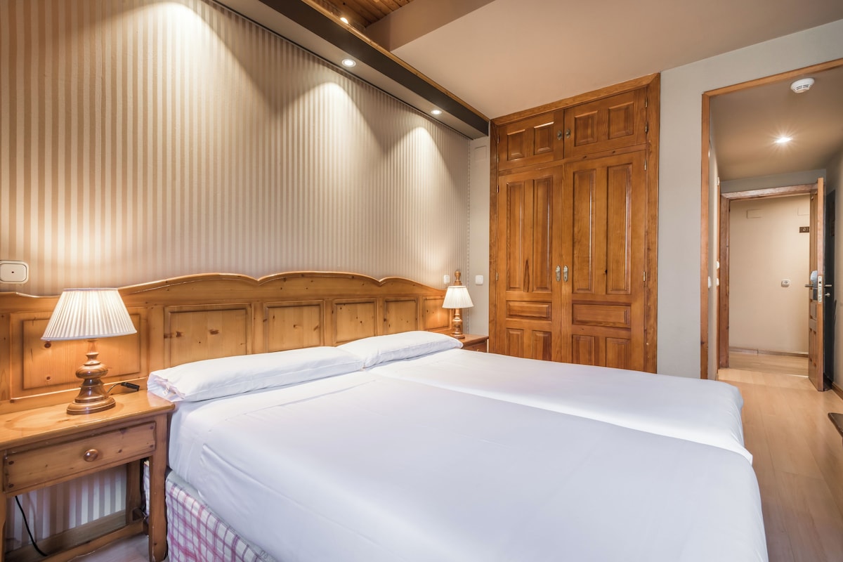 A hotel room with a large bed, wooden headboard, two bedside tables with lamps, and a wardrobe.