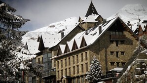 A traditional chalet-style building with multiple steeply pitched roofs, surrounded by snow-covered trees and mountains in the background. - Villa De Sallent 3 (Sallent de Gallego)