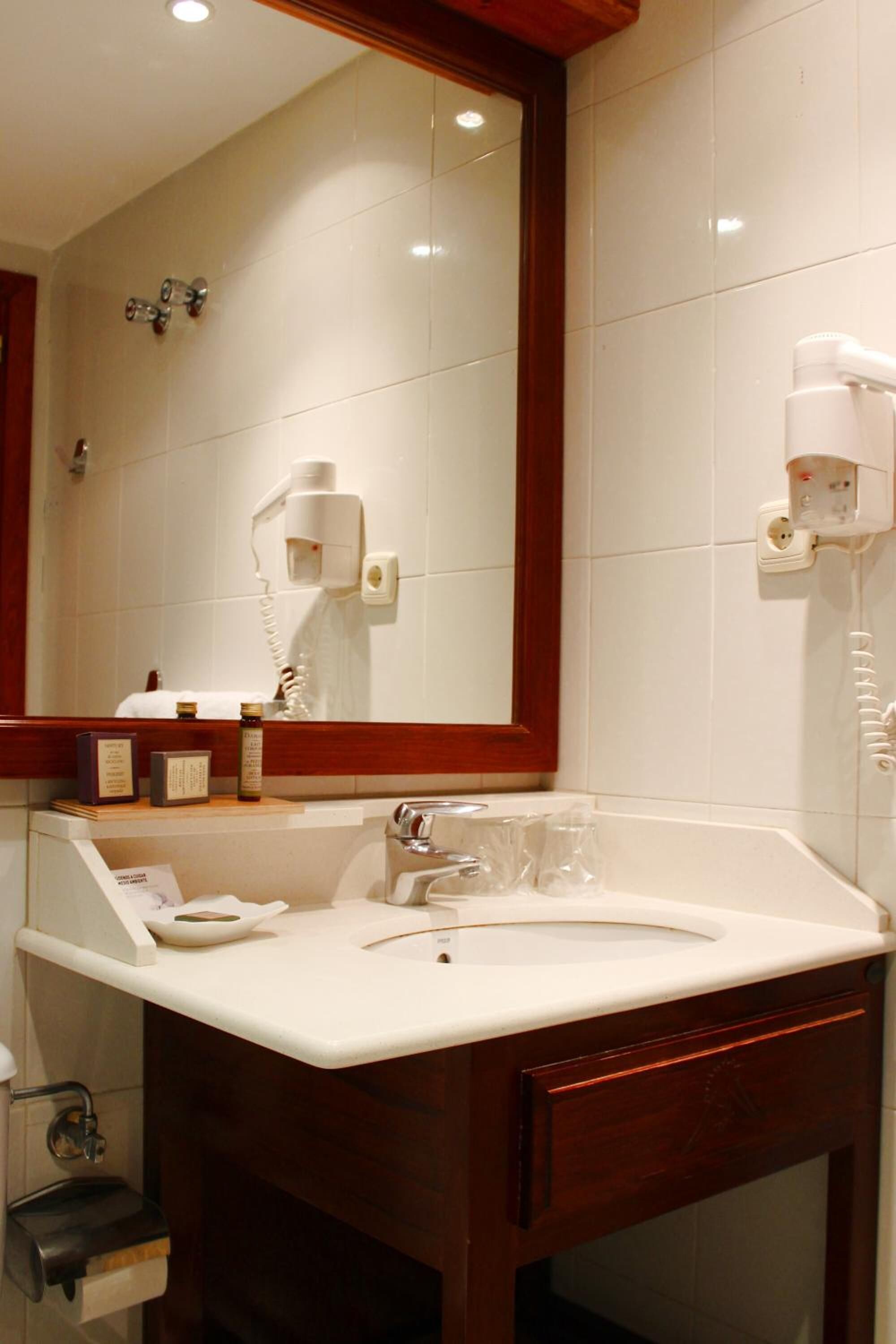 A bathroom with a large mirror, a sink, and a hairdryer mounted on the wall.