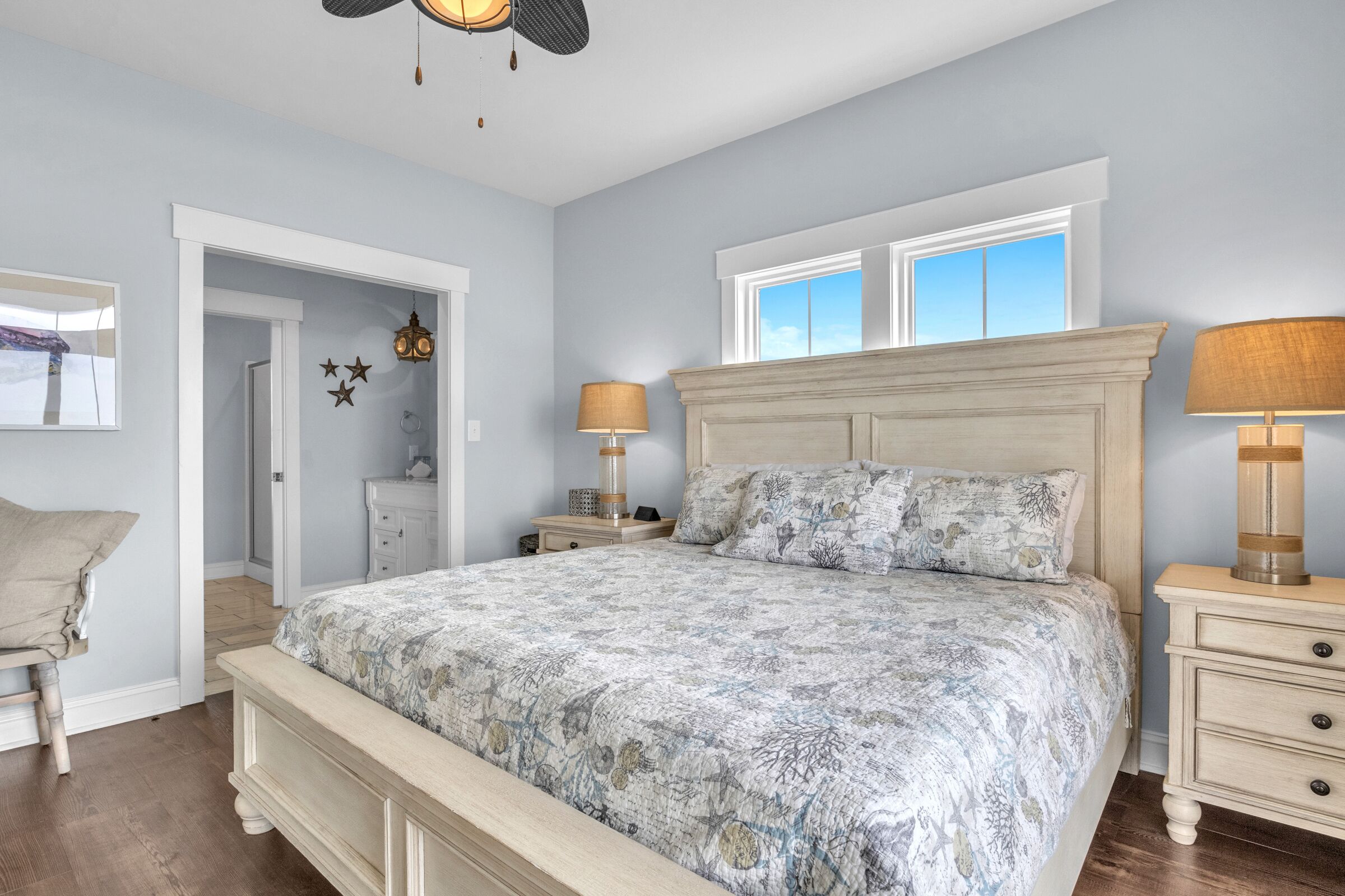 A bedroom with a large bed, two bedside lamps, a nightstand, a dresser, and a window with a view.