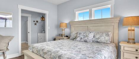 A bedroom with a large bed, two bedside lamps, a nightstand, a dresser, and a window with a view.