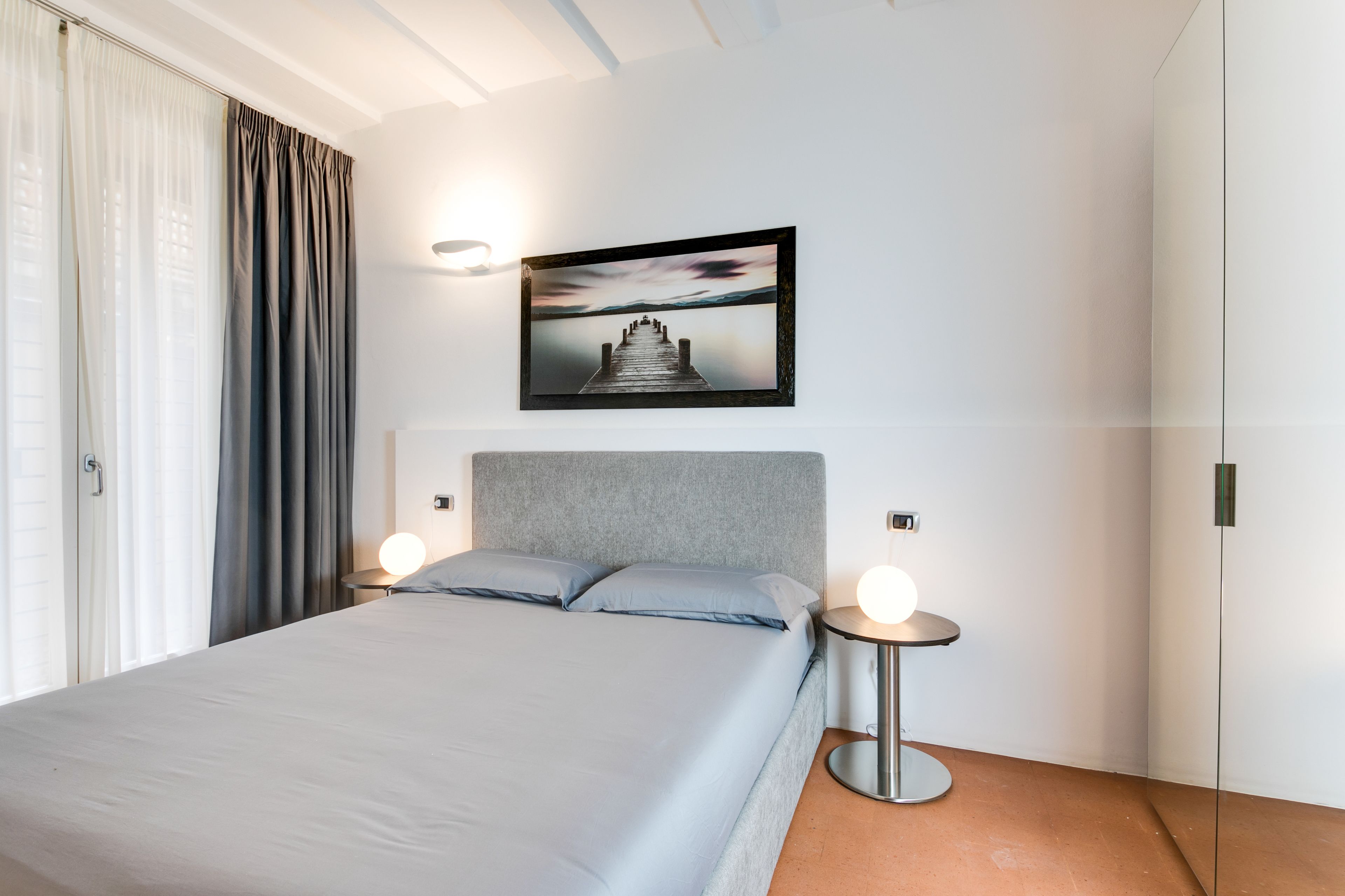 A modern bedroom with a bed, a headboard, a bedside table with a lamp, and a framed picture on the wall.