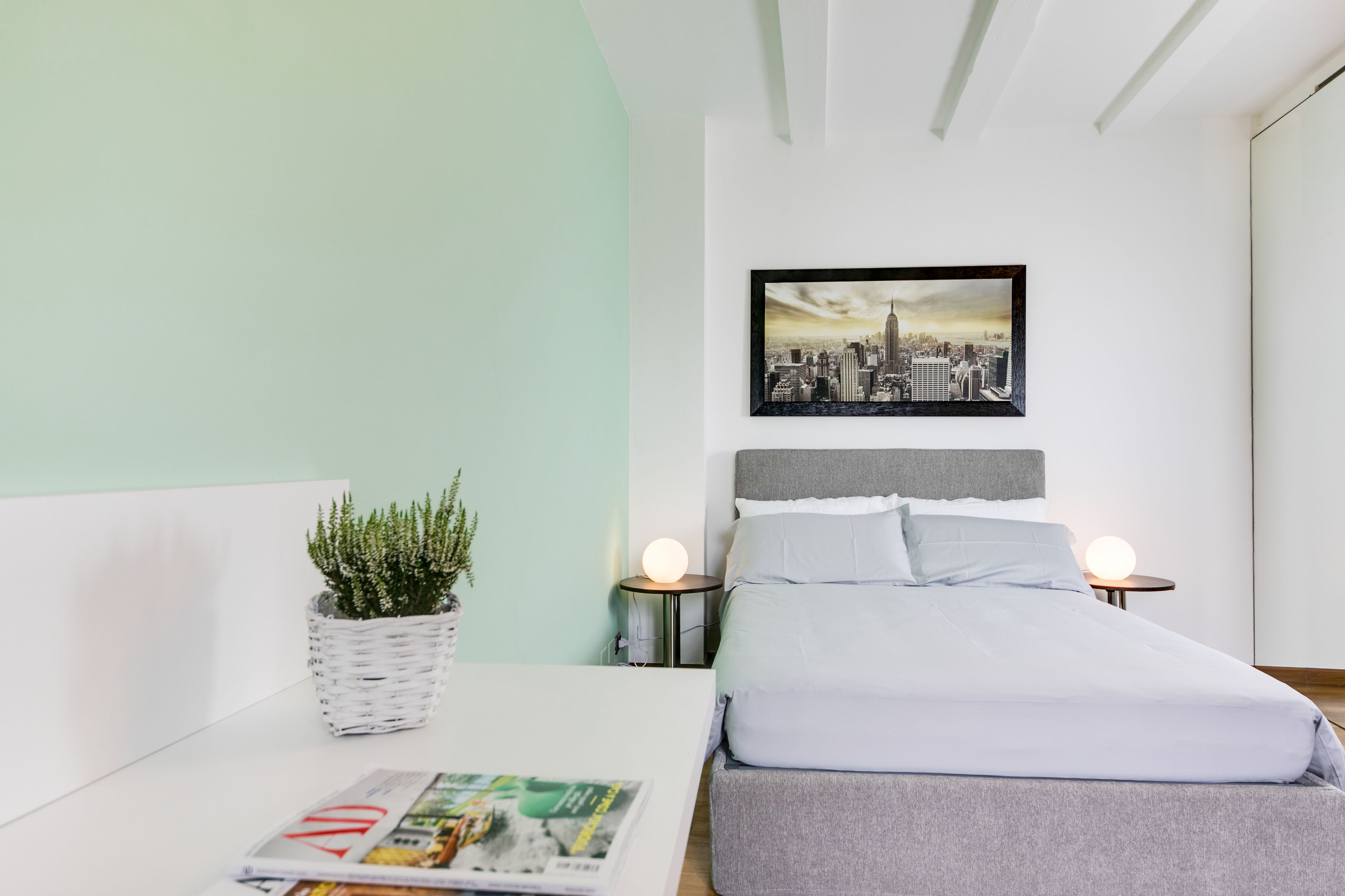 Een netjes ingerichte slaapkamer met een bed, nachtkastjes, een aan de muur bevestigd schilderij en een potplant.