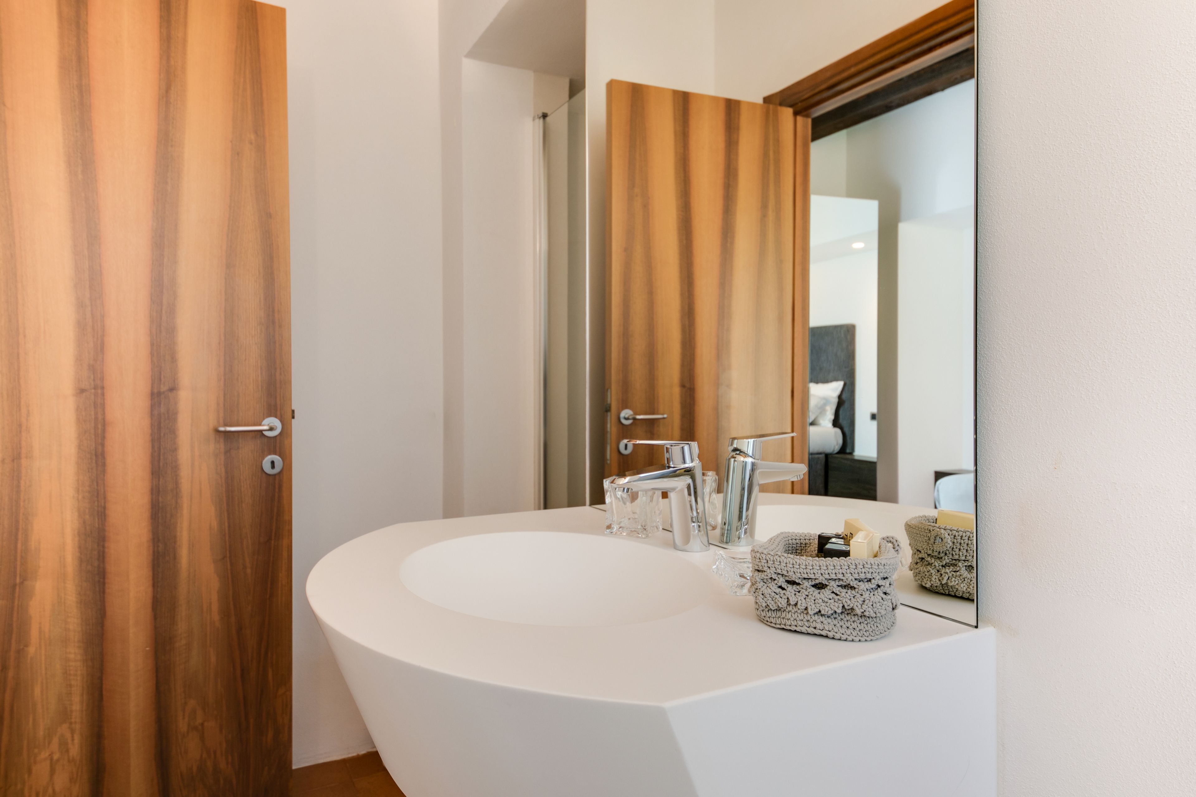 A modern bathroom with a white sink, two chrome faucets, and a wooden door.