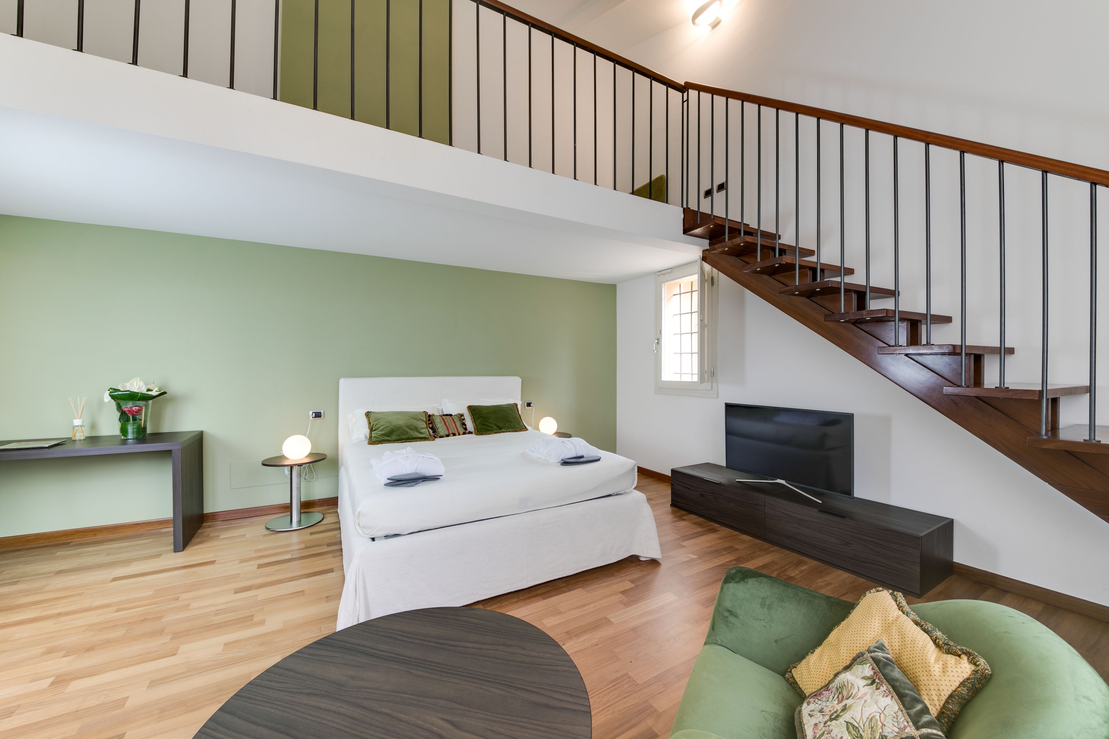 A bedroom with a bed, bedside table, lamp, and a TV stand.