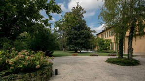A courtyard with a gravel path, stone wall, and lush greenery including trees and flowering plants.