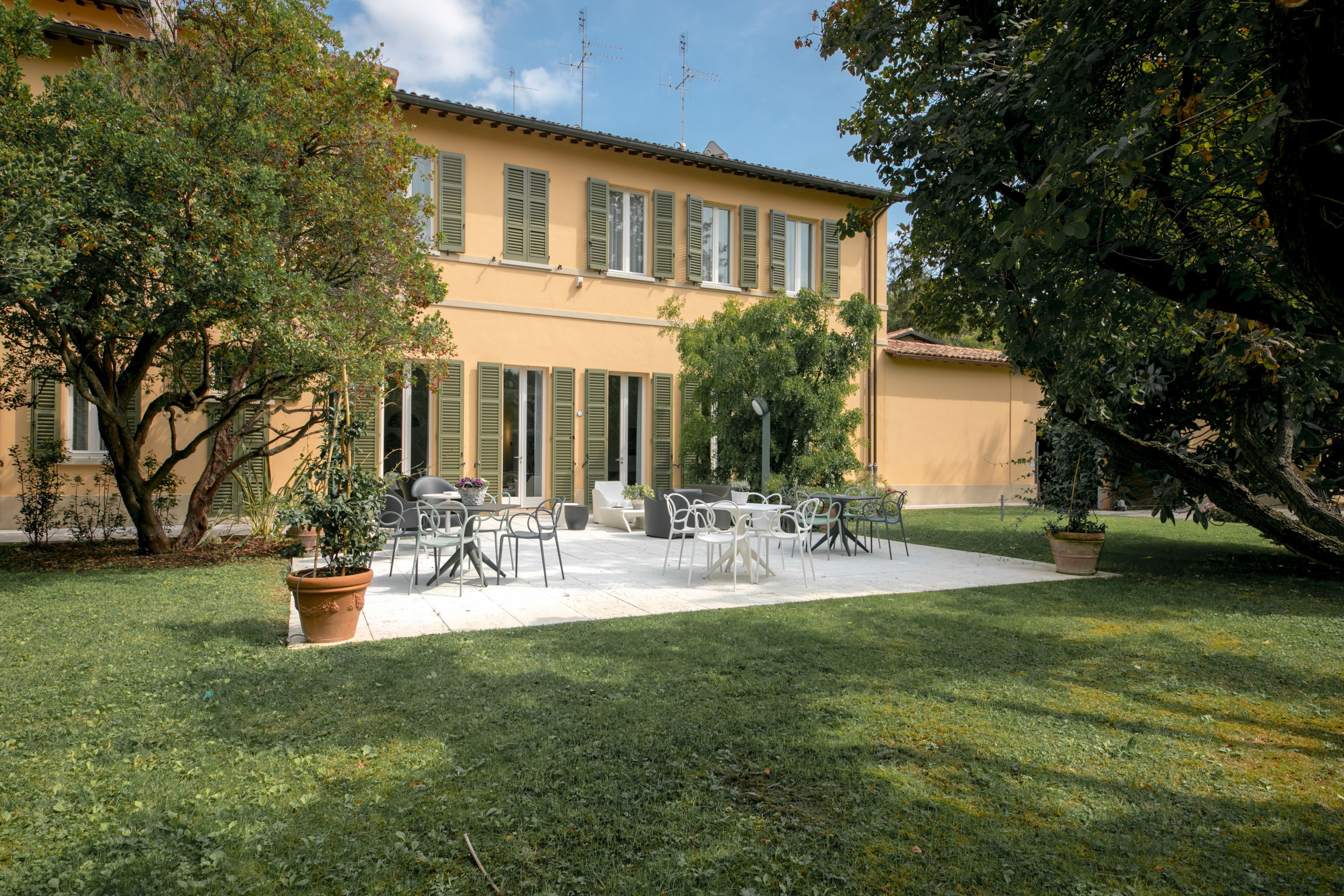 A courtyard with outdoor seating, a building with shutters, and a large tree.
